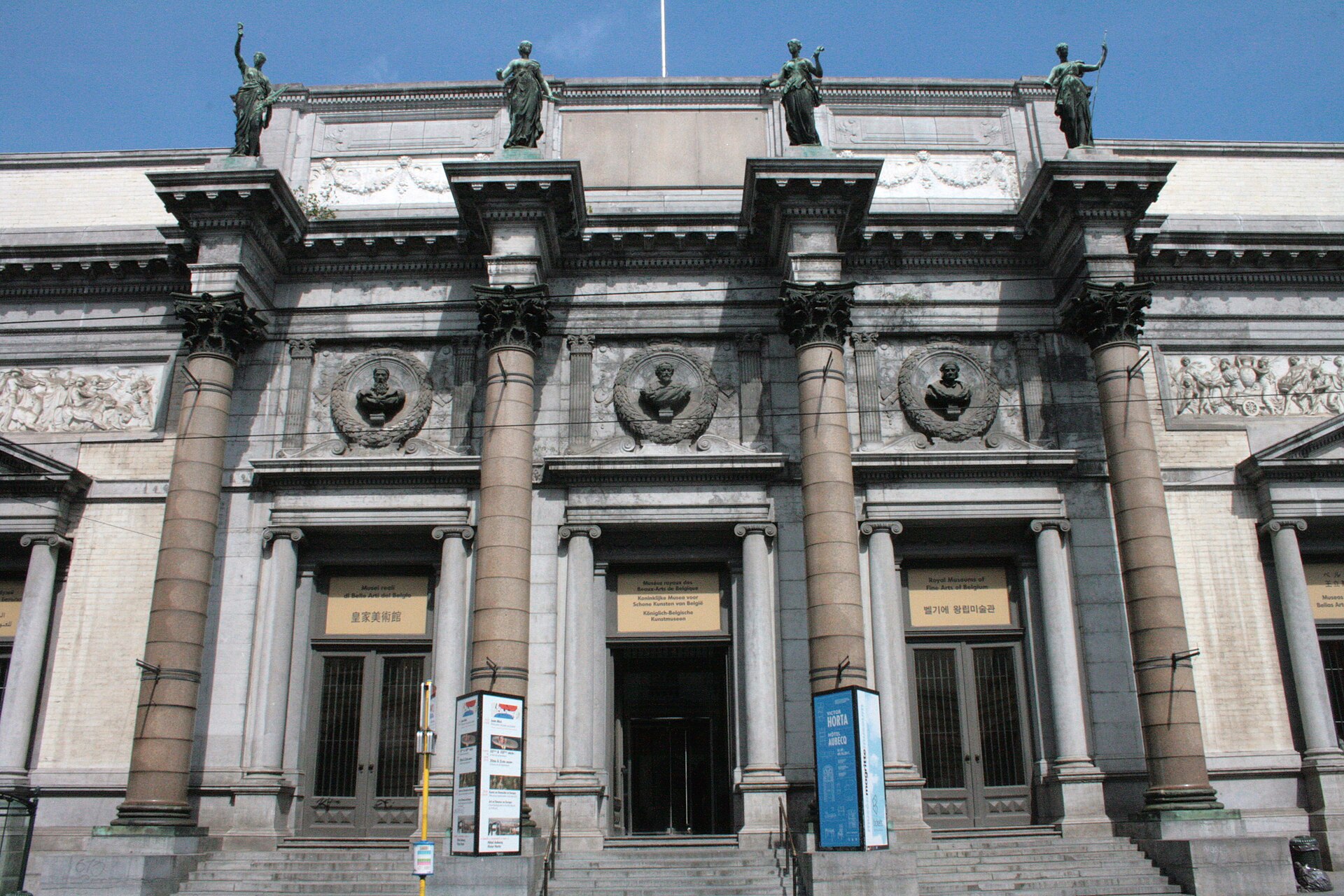 Four stone columns frame the entrance to the Royal Museums of Fine Arts of Belgium in Brussels beneath bronze statues.