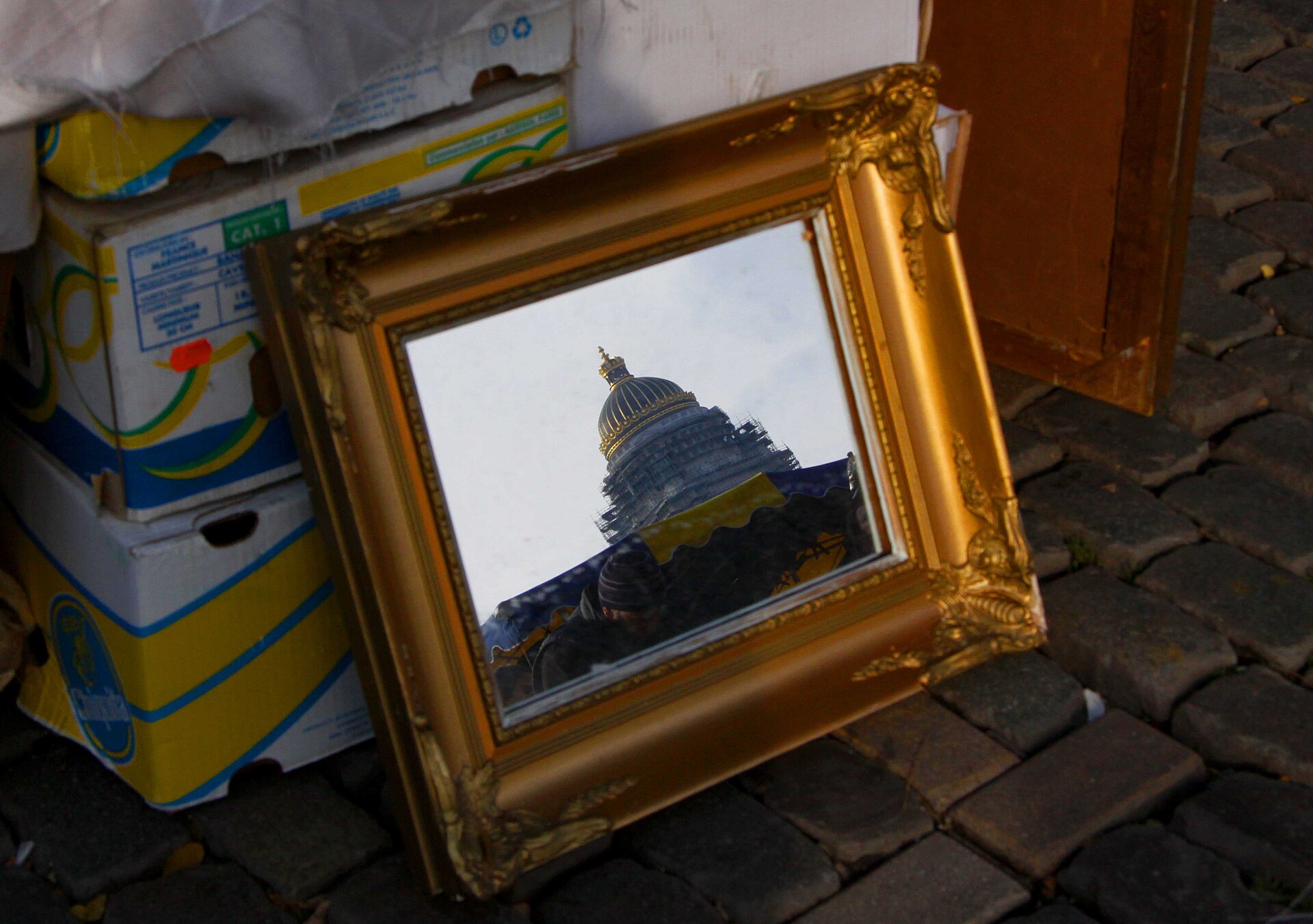 A gold framed mirror for sale at Brussels Jeu de Balle flea market reflects the domed Palace of Justice above the stalls.