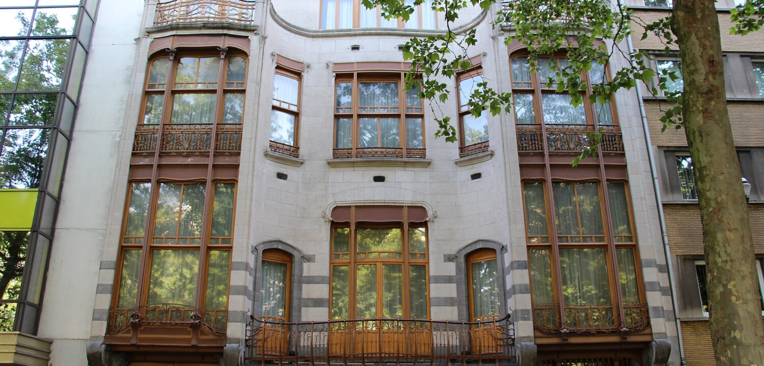 Hotel Solvay in Brussels features curved stone bays, tall wooden windows and delicate iron balconies beneath leafy street trees.