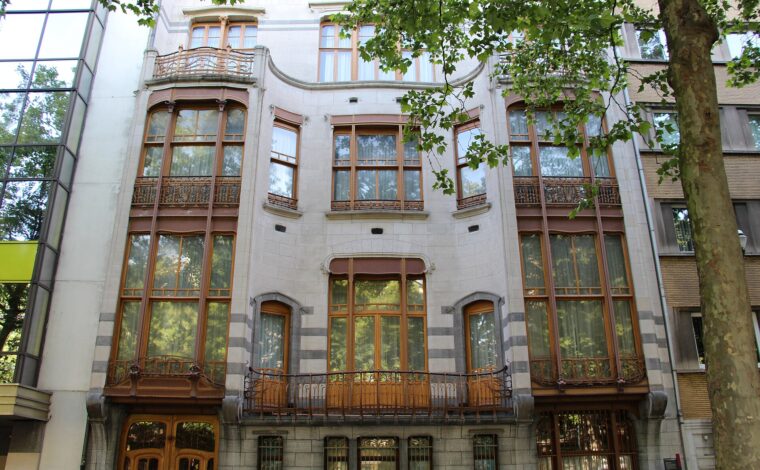 Hotel Solvay in Brussels features curved stone bays, tall wooden windows and delicate iron balconies beneath leafy street trees.