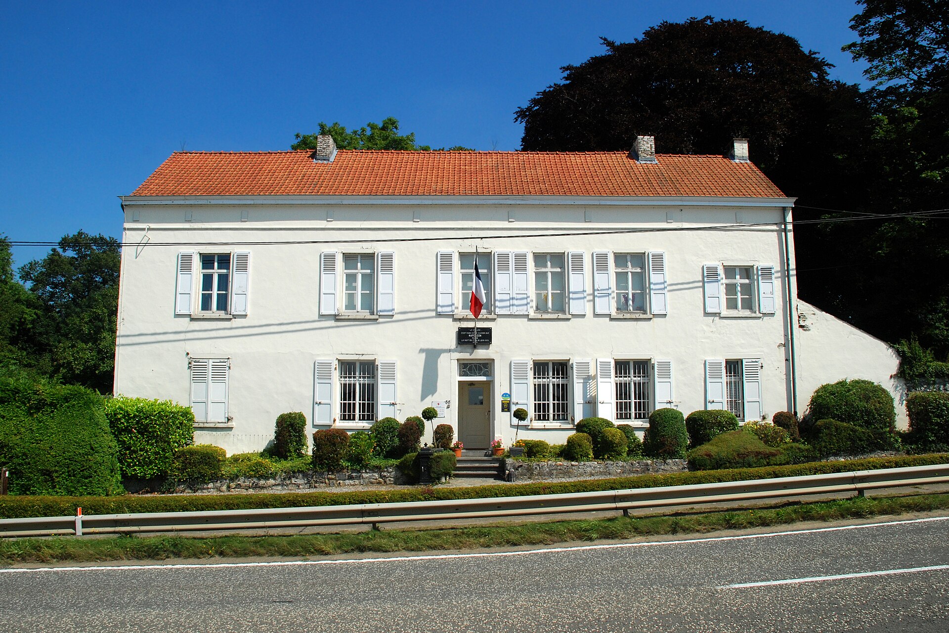 Le Caillou near Waterloo has a white farmhouse façade, pale shutters, a red tiled roof and a French flag.