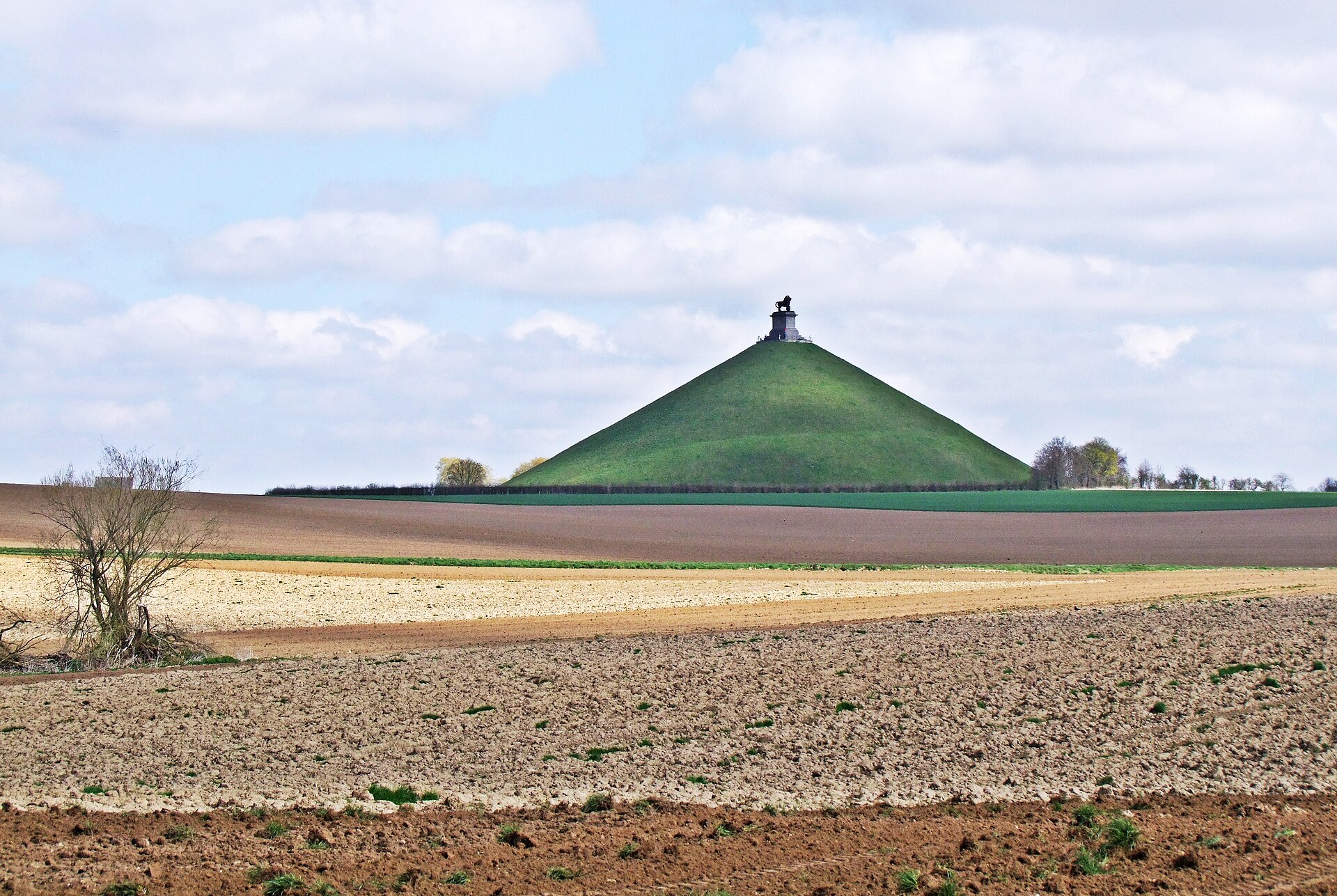 The Lion’s Mound rises above ploughed fields on the Waterloo battlefield beneath a lightly clouded spring sky.