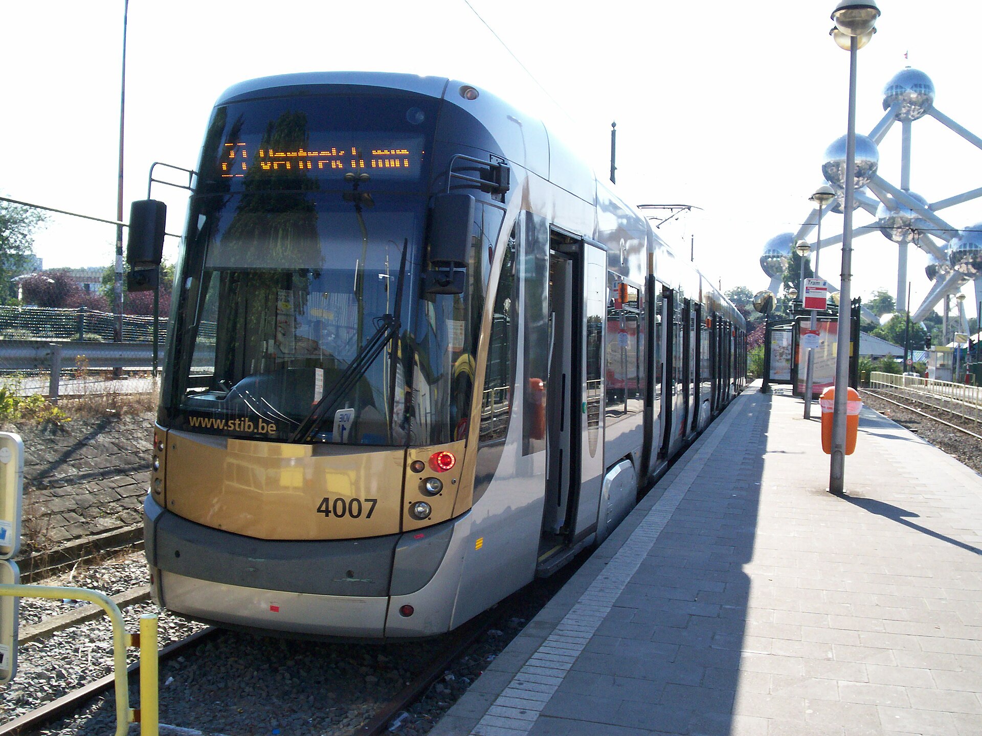 A low-floor STIB tram stands beside a paved platform and tactile strip at Heysel, with Brussels’ Atomium behind.