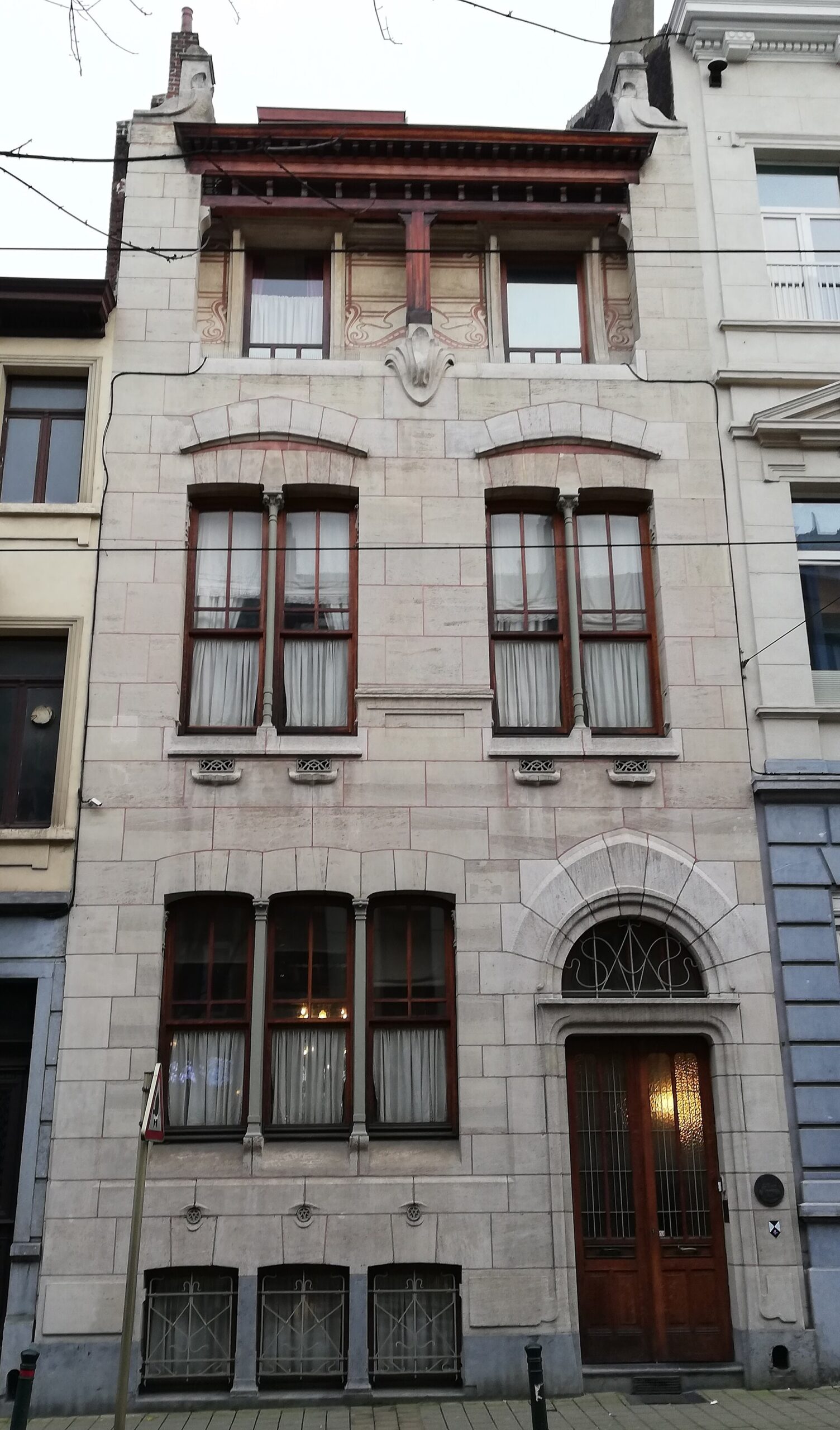 Maison Autrique in Schaerbeek, Brussels, with tall paired windows, a curved entrance arch and decorative panels beneath the roof.