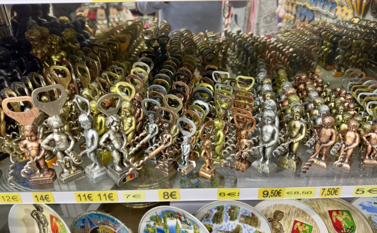 Manneken Pis bottle openers and corkscrews fill a Brussels souvenir shop display above colourful Belgian souvenir plates.