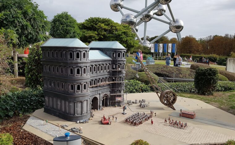 Mini-Europe's model of Trier's Porta Nigra stands beside tiny Roman figures, with visitors and the Atomium behind in Brussels.
