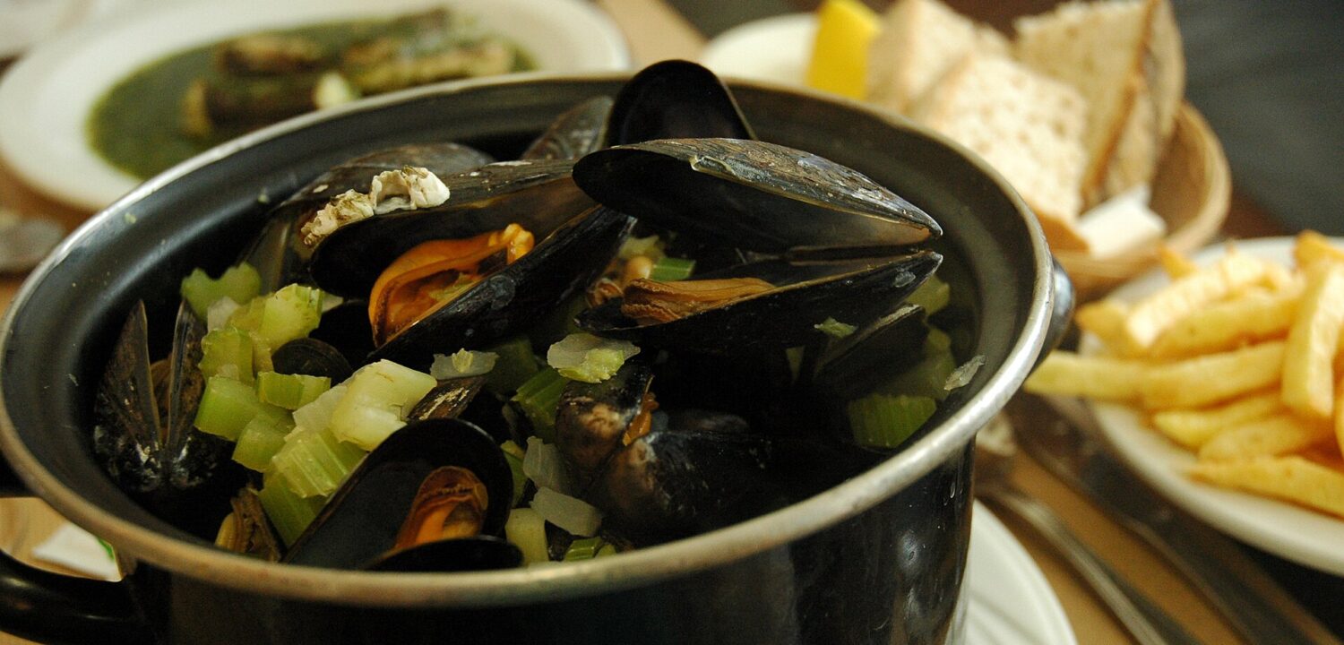 Mussels and chopped celery fill a black pot at Au Pre Sale in Brussels, with fries and sliced bread alongside.