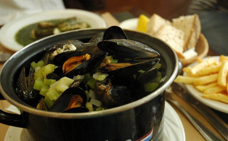 Mussels and chopped celery fill a black pot at Au Pre Sale in Brussels, with fries and sliced bread alongside.