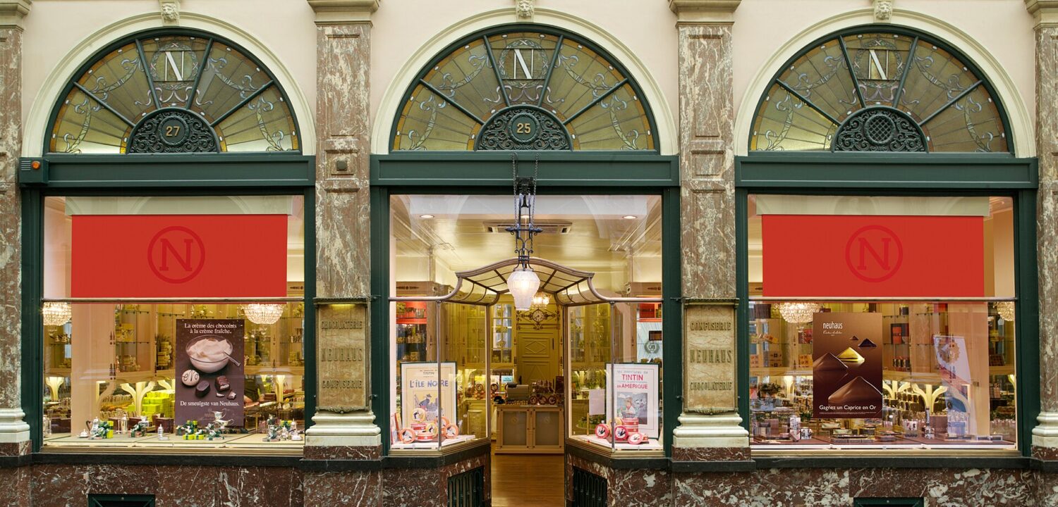 Neuhaus chocolate shop in Brussels Galerie de la Reine has arched windows, red blinds and an open central doorway.