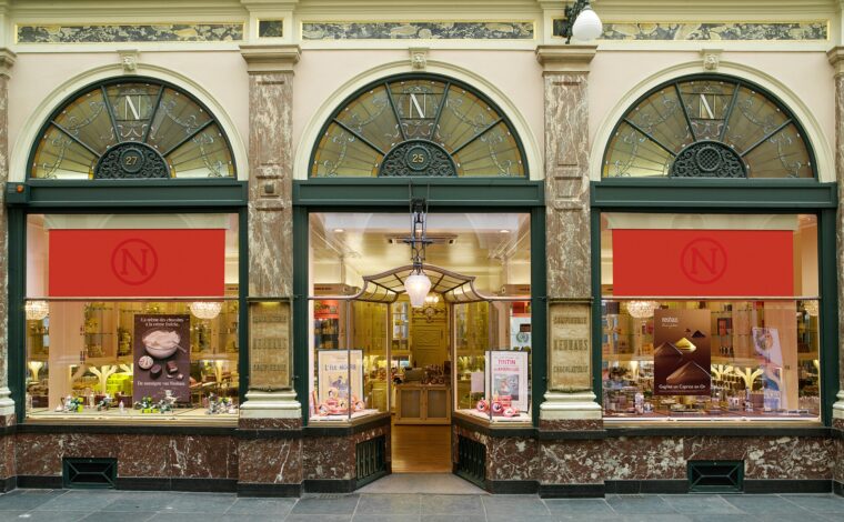 Neuhaus chocolate shop in Brussels Galerie de la Reine has arched windows, red blinds and an open central doorway.