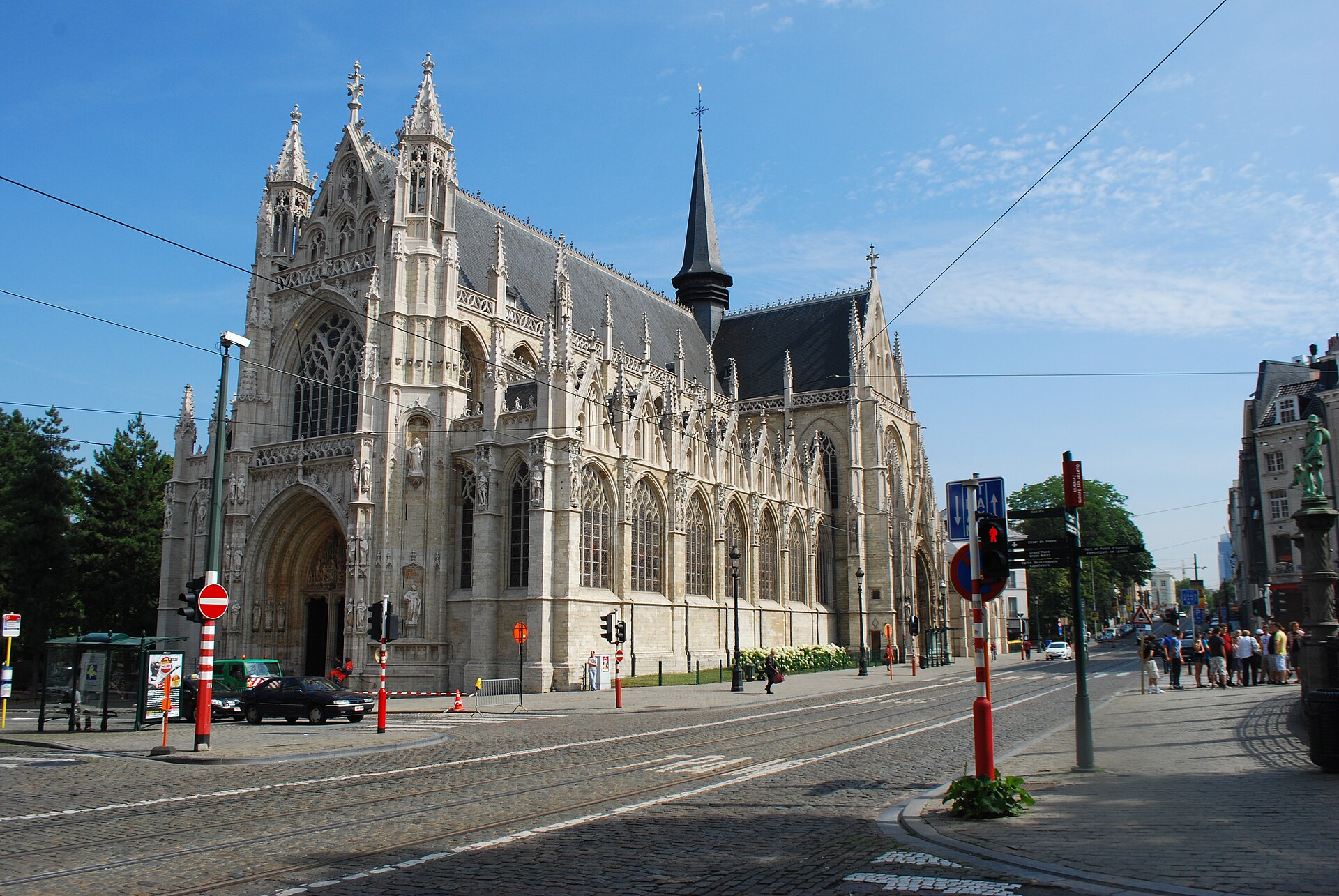 Notre-Dame du Sablon rises beside tram tracks in Brussels, with ornate Gothic windows and a slender dark spire.