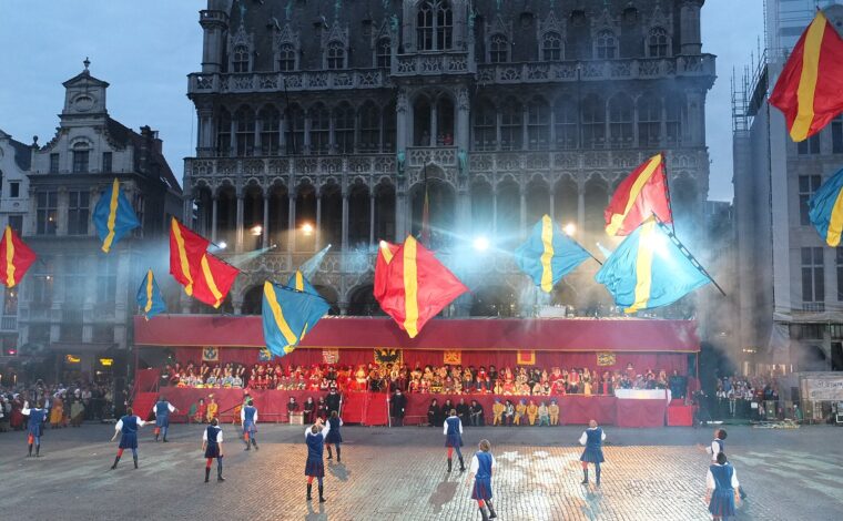 Ommegang flag throwers in blue costumes send red and blue flags above Brussels Grand-Place, with the Maison du Roi behind.