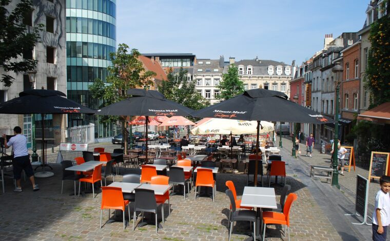 Orange and grey chairs surround outdoor cafe tables beneath umbrellas on Rue de l Epee in the Marolles district of Brussels.