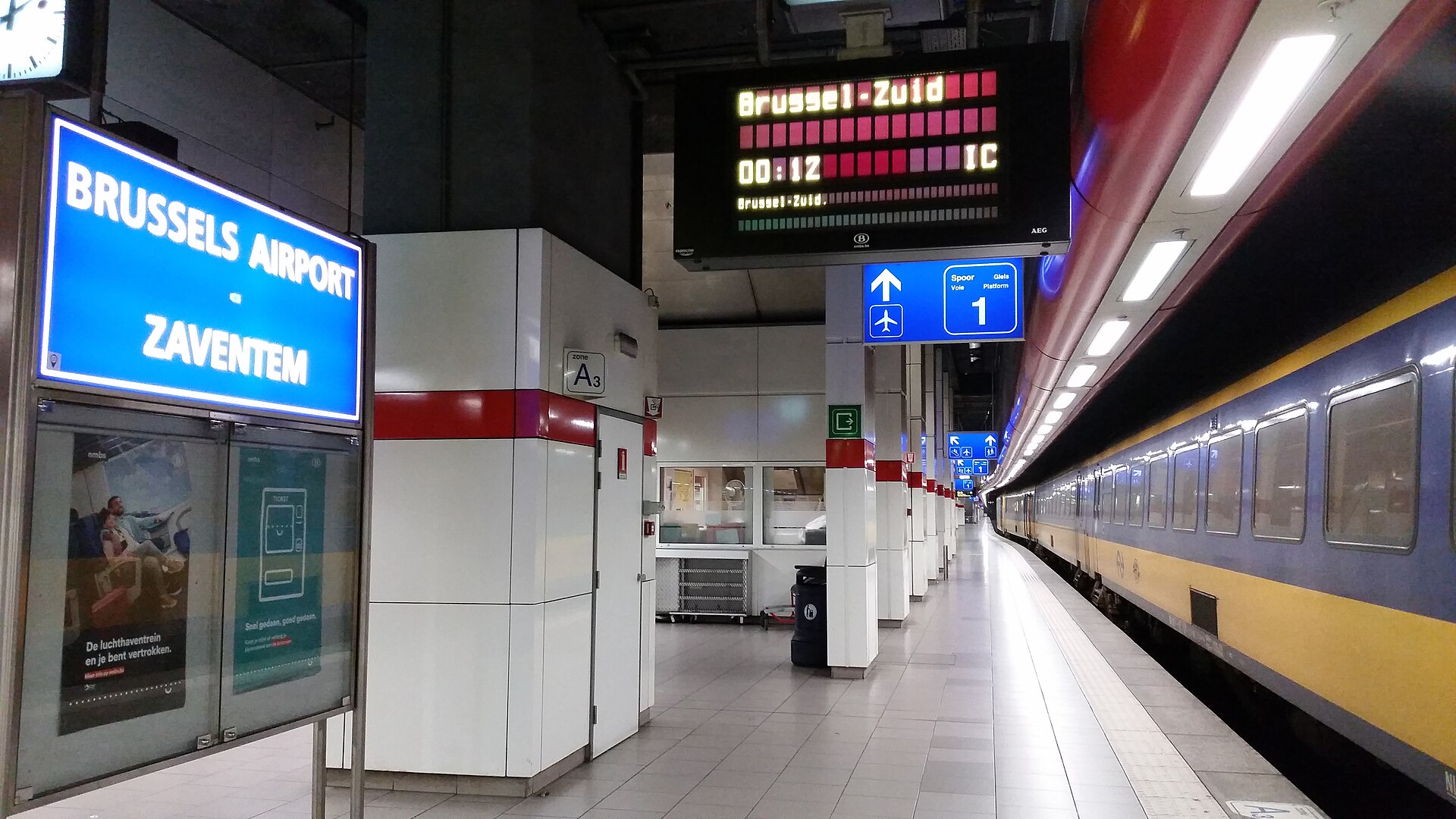 A passenger train waits beside the Brussels Airport Zaventem station sign and a departure display for Brussels-South.