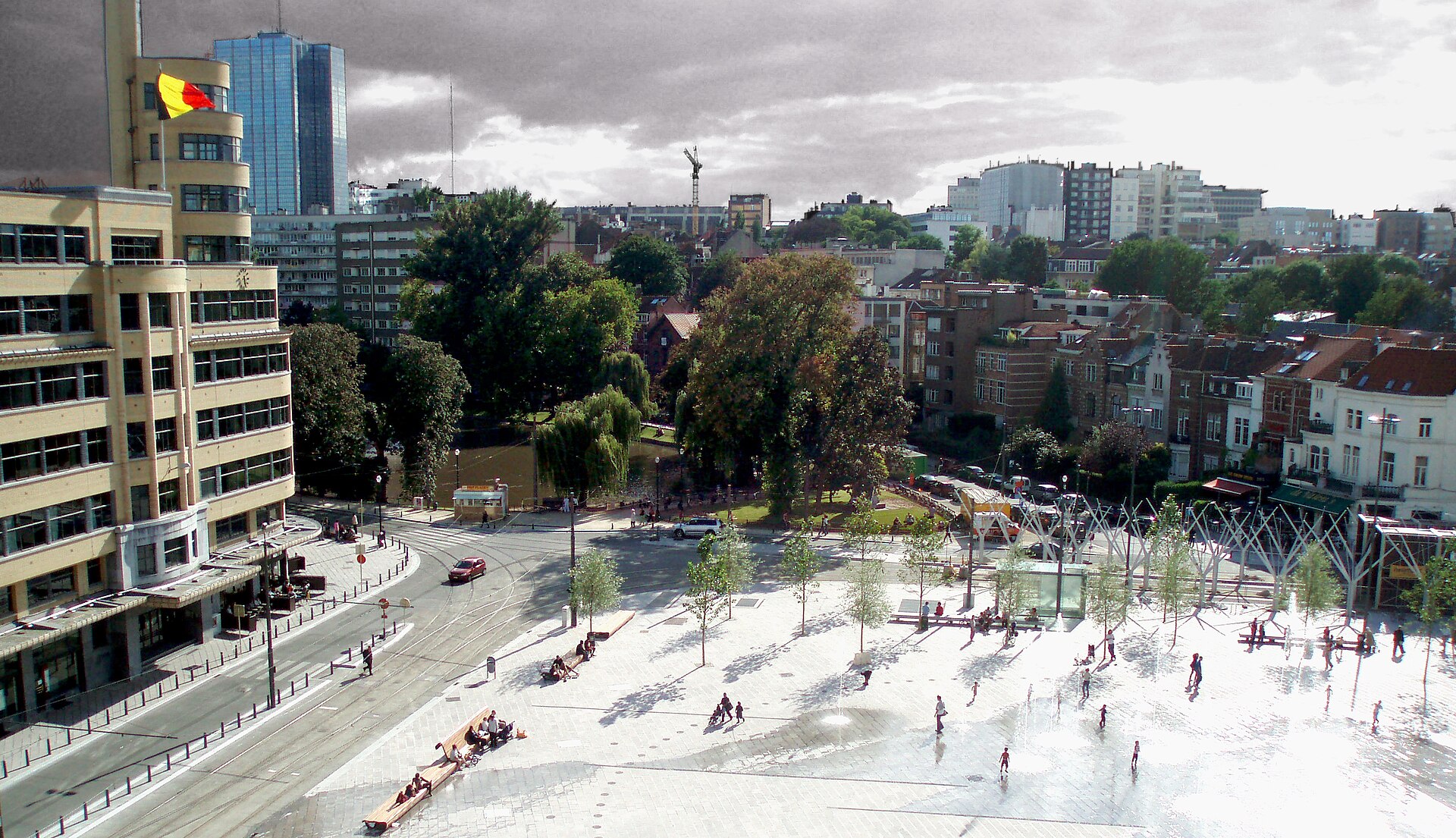 People gather around fountains on Place Flagey in Ixelles, Brussels, beside the rounded Art Deco Flagey building and tram shelter.