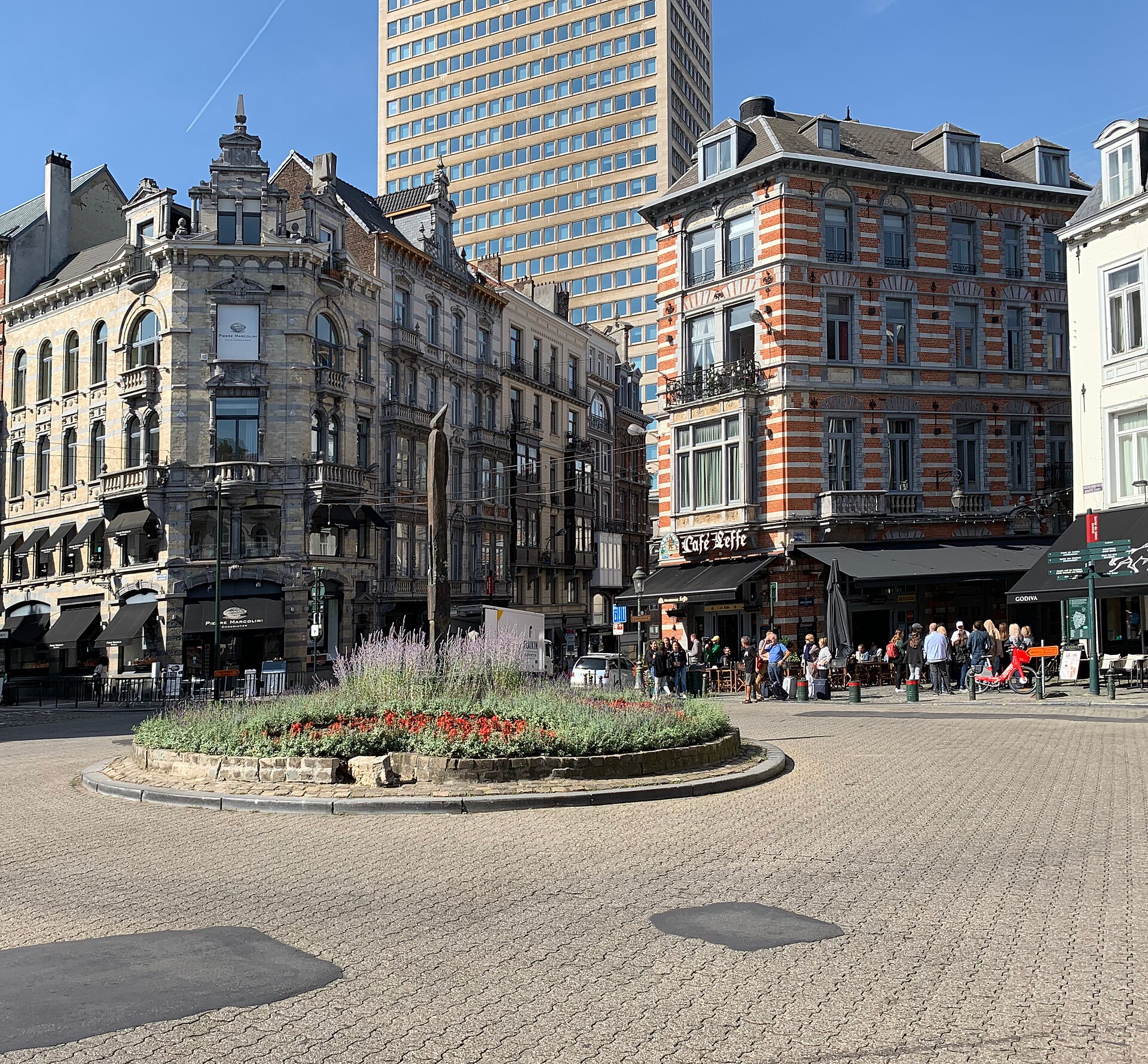 Place du Grand Sablon in Brussels has a planted island, ornate corner buildings, chocolate shops and people gathered outside a cafe.