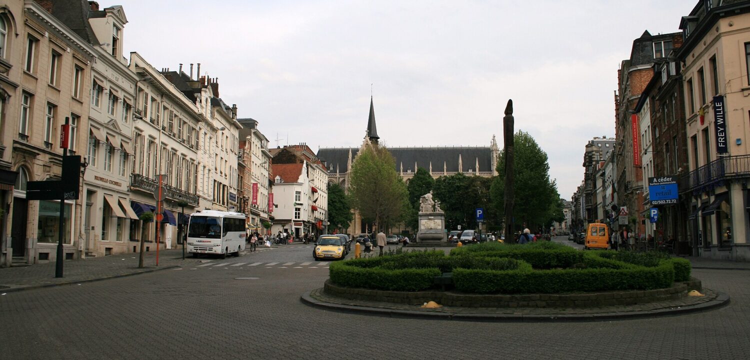 Place du Grand Sablon in Brussels stretches between historic facades toward Notre-Dame du Sablon, behind trees and a stone fountain.