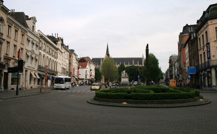 Place du Grand Sablon in Brussels stretches between historic facades toward Notre-Dame du Sablon, behind trees and a stone fountain.