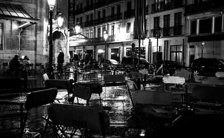 Rain glistens on outdoor tables at Zebra Bar on Place Saint-Gery in Brussels, with customers beneath illuminated street lamps.