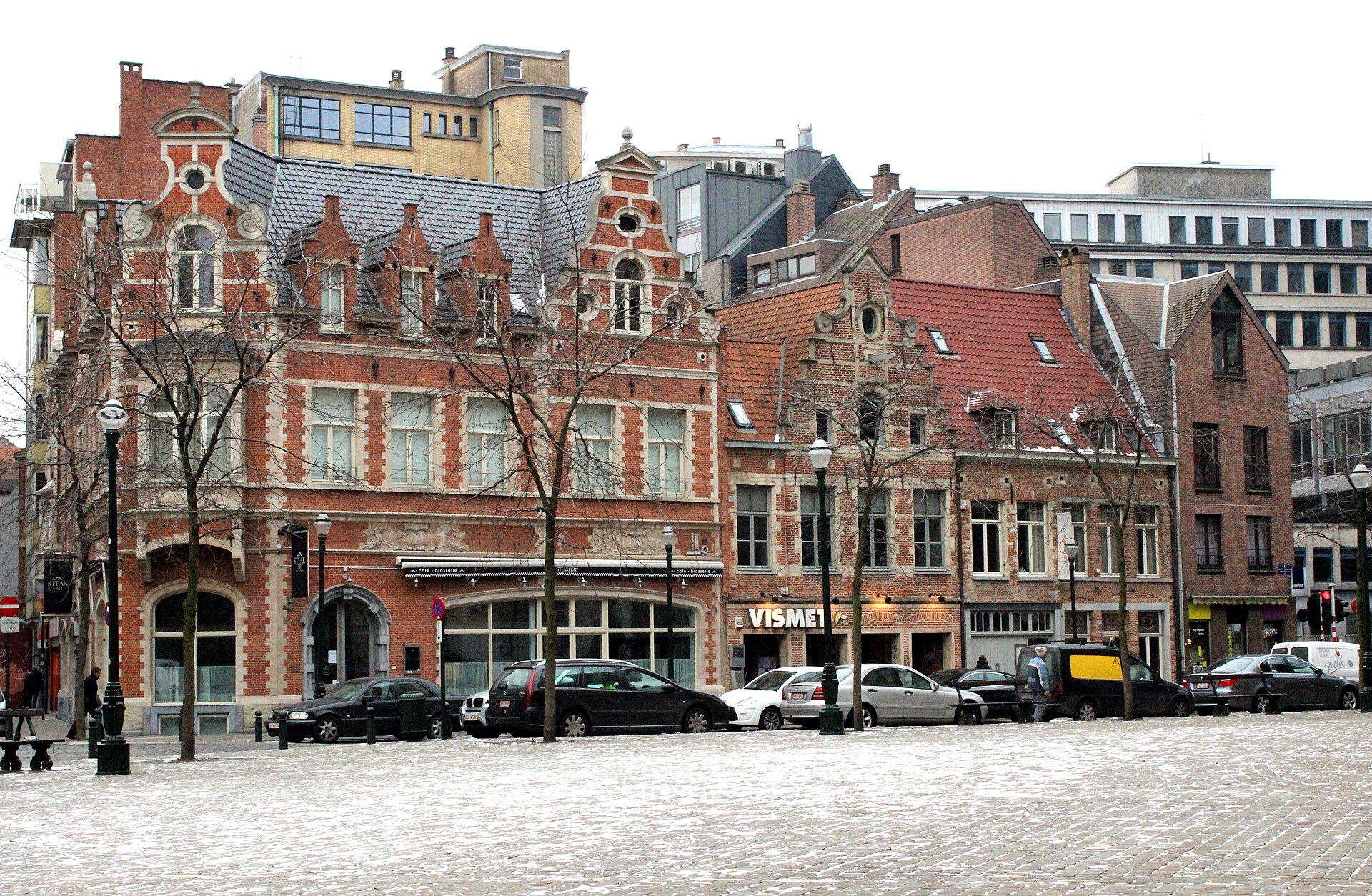 Red brick gabled buildings and the Vismet restaurant face a lightly snow covered square behind Sainte-Catherine church in Brussels.