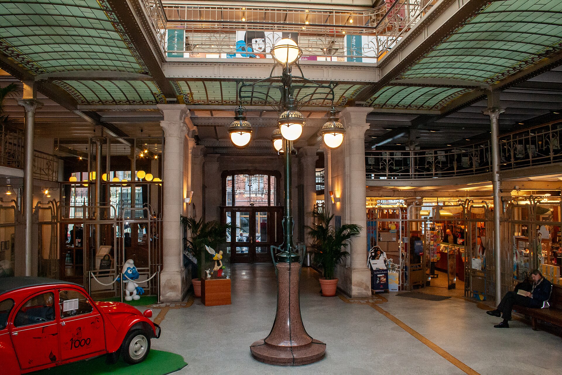 A red display car and comic character figures decorate the Belgian Comic Strip Centre hall in Brussels beneath ornate lamps.