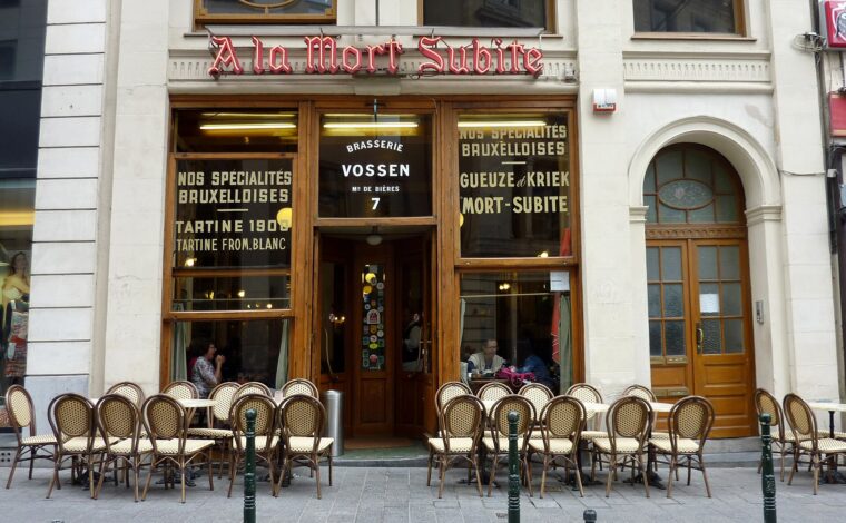 Red lettering marks Brussels A la Mort Subite above wooden windows advertising gueuze and kriek, with cafe chairs outside.