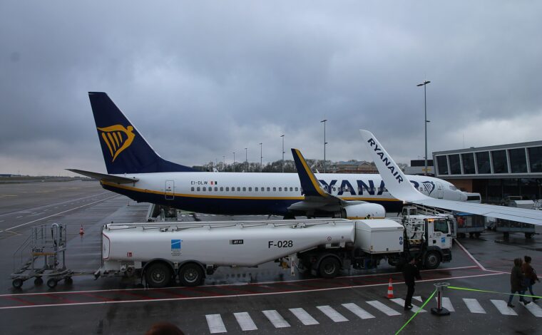 Ryanair aircraft stand beside Charleroi Airport terminal while a branded fuel tanker and walking passengers occupy the wet apron.