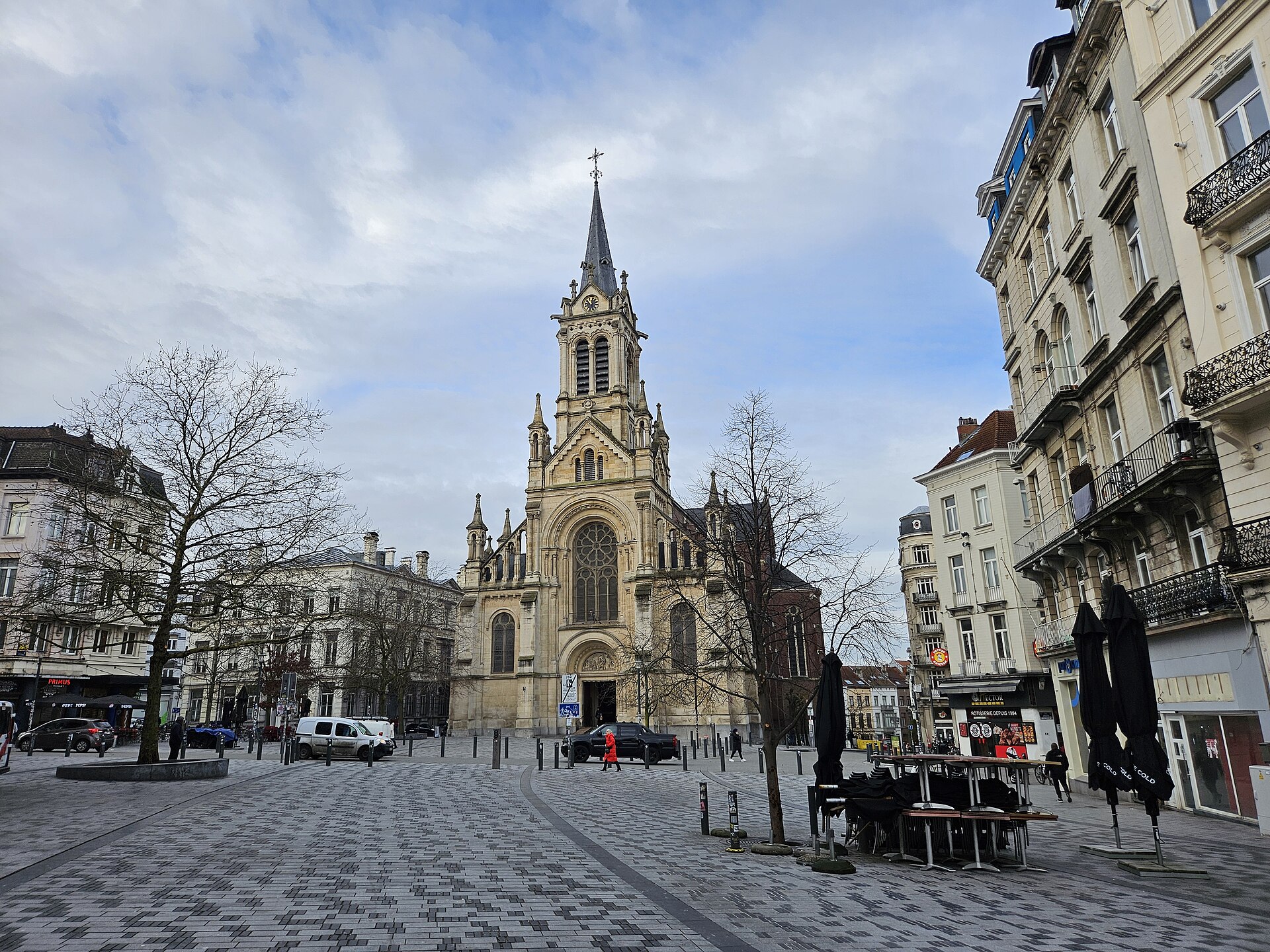 Saint-Gilles church overlooks the patterned paving of the Parvis de Saint-Gilles in Brussels, with cafe terraces and bare trees beside it.