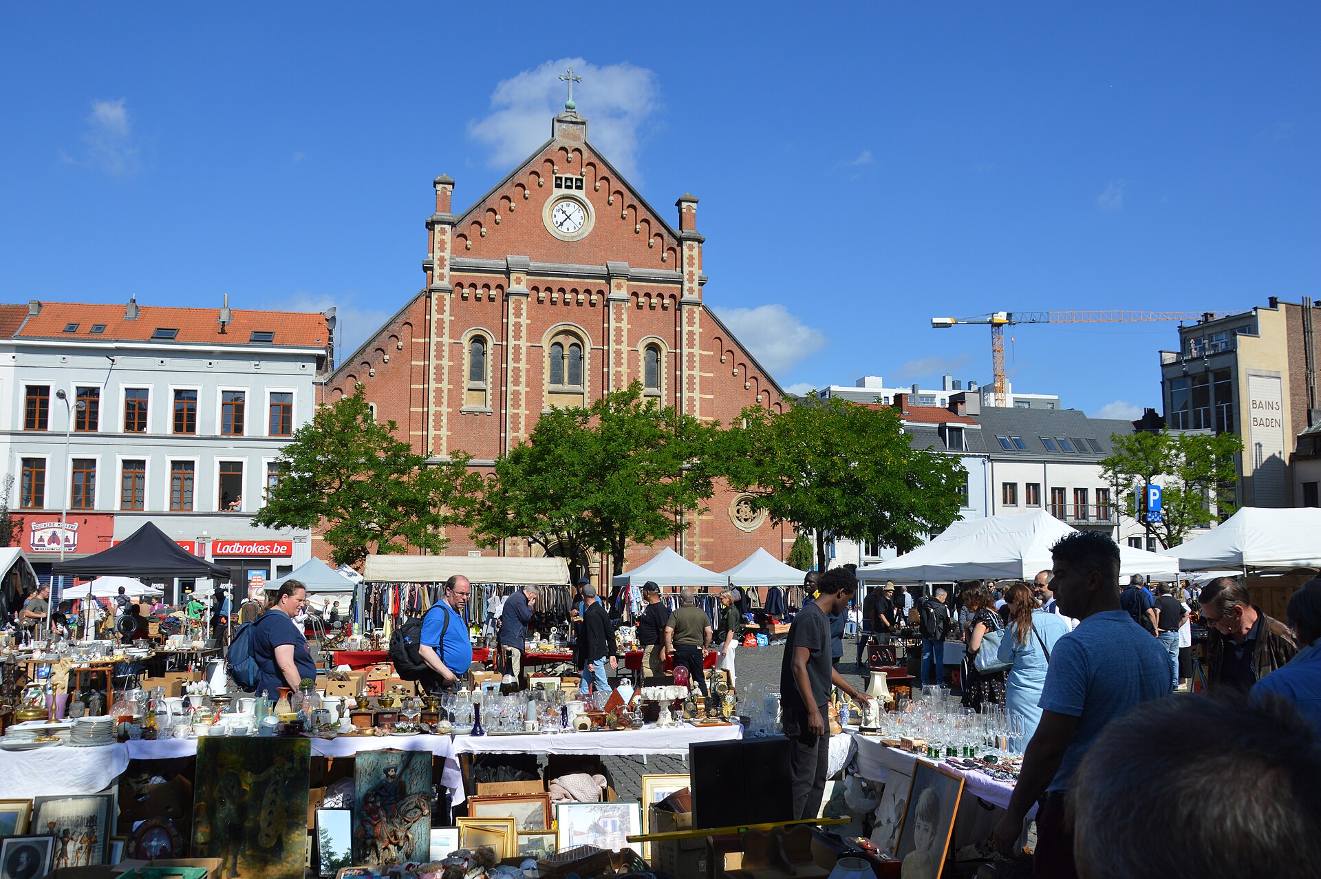 Shoppers browse glassware and framed pictures at Place du Jeu de Balle in Brussels beneath the red brick church and white market canopies.