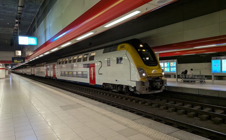 A silver SNCB double-deck train with red doors stands beside the underground platform at Brussels Airport Zaventem station.