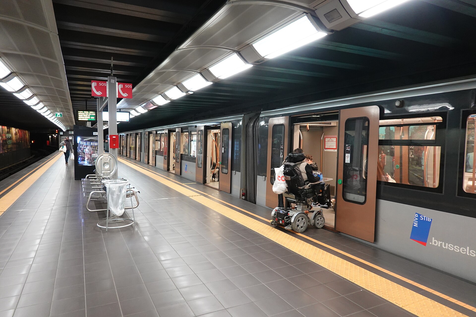 A silver STIB metro train opens its doors at CERIA/COOVI in Brussels as passengers wait beside the platform.