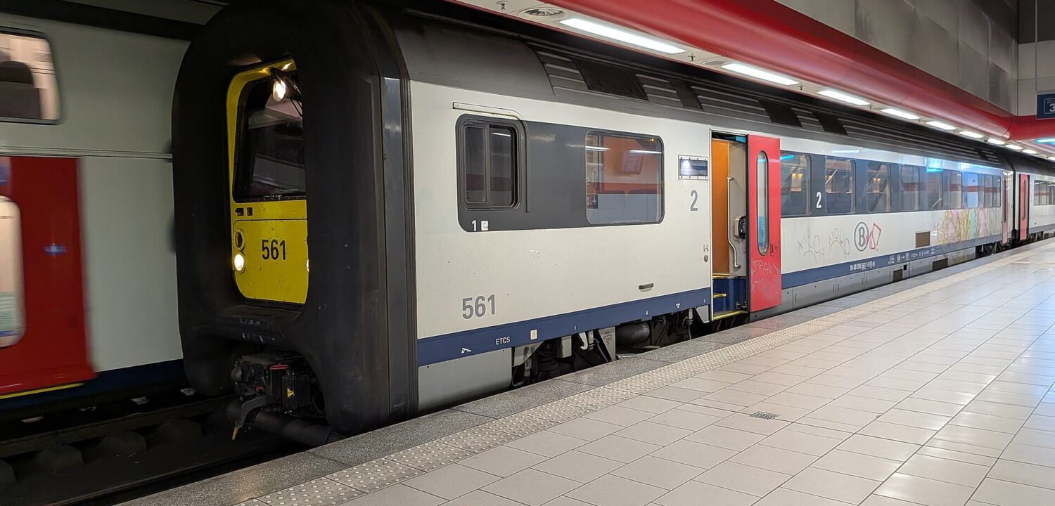 An SNCB train numbered 561 stands with a red door open beside the platform at Brussels Airport Zaventem station.