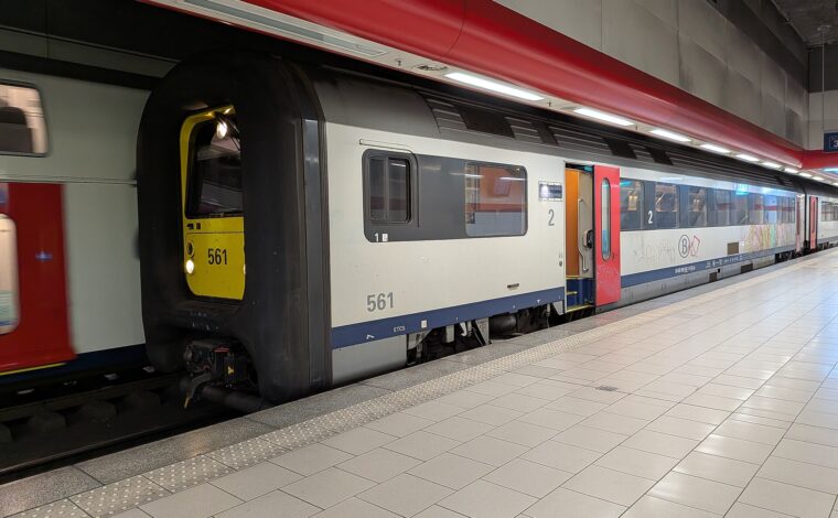 An SNCB train numbered 561 stands with a red door open beside the platform at Brussels Airport Zaventem station.