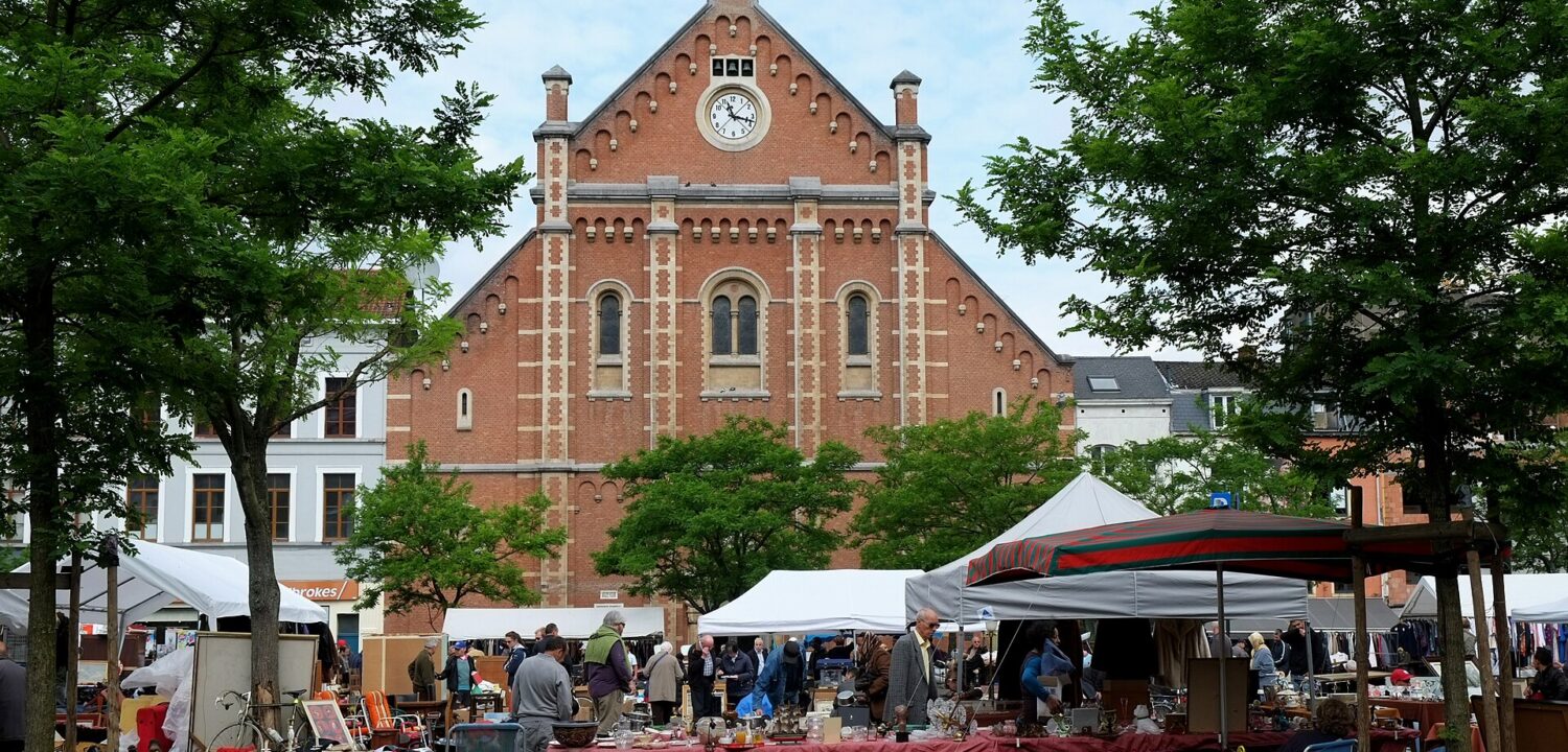 Stalls and secondhand household goods fill Place du Jeu de Balle in Brussels beneath the red brick church and leafy trees.