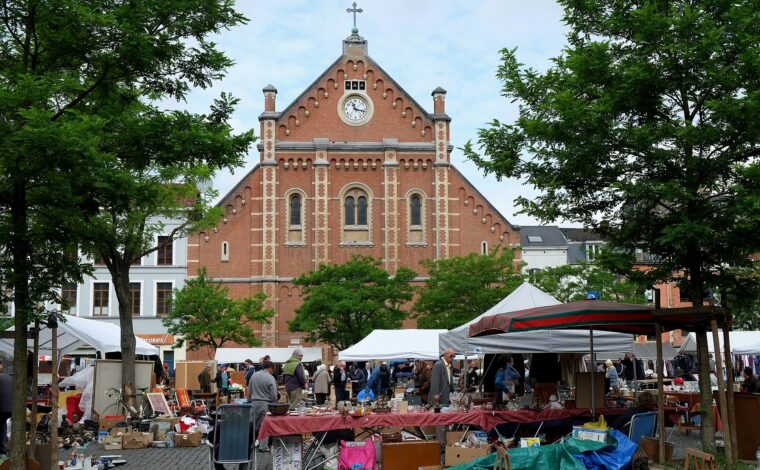 Stalls and secondhand household goods fill Place du Jeu de Balle in Brussels beneath the red brick church and leafy trees.