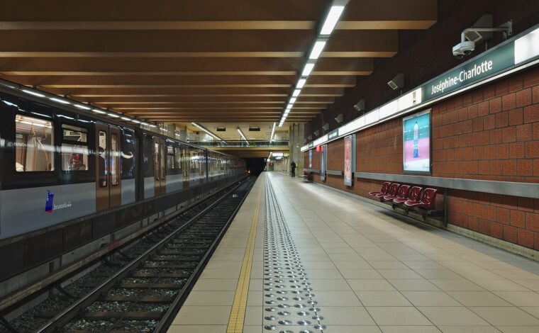 A STIB metro train stands beside the signed Joséphine-Charlotte platform in Brussels, with red seats along the brick wall.