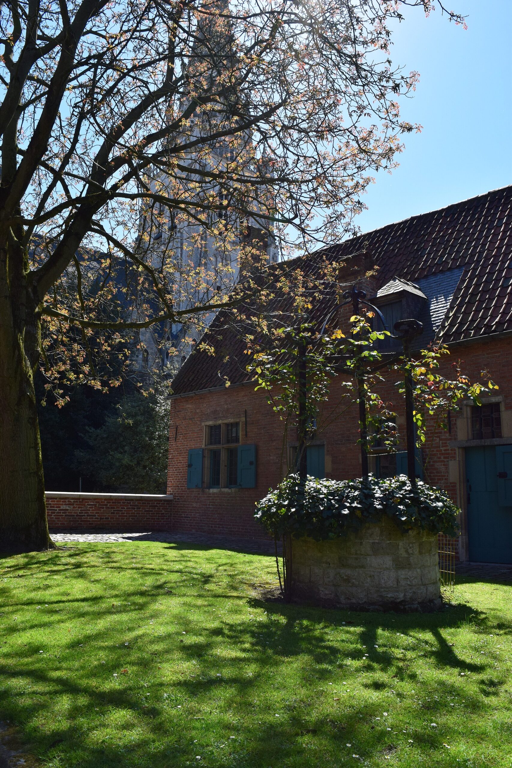 A stone well stands in the grassy courtyard of Anderlecht Beguinage in Brussels, beside cottages with green shutters.