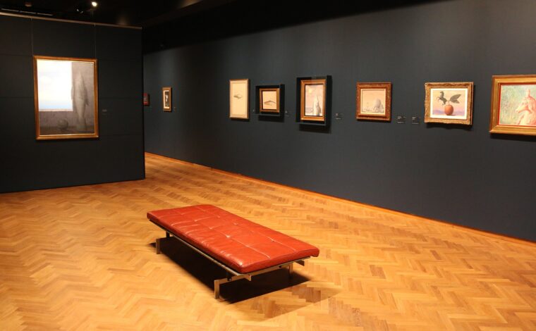Surrealist paintings line dark walls around a red leather bench inside the Magritte Museum in Brussels, above patterned parquet flooring.