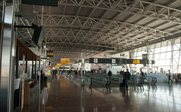 Travellers pass gate seating and moving walkways beneath the steel-truss roof of Brussels Airport Terminal A.