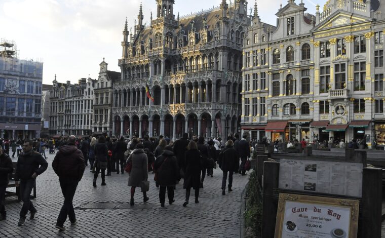 Visitors cross the Grand-Place in Brussels in front of the Gothic Maison du Roi and neighbouring gilded guildhouses.