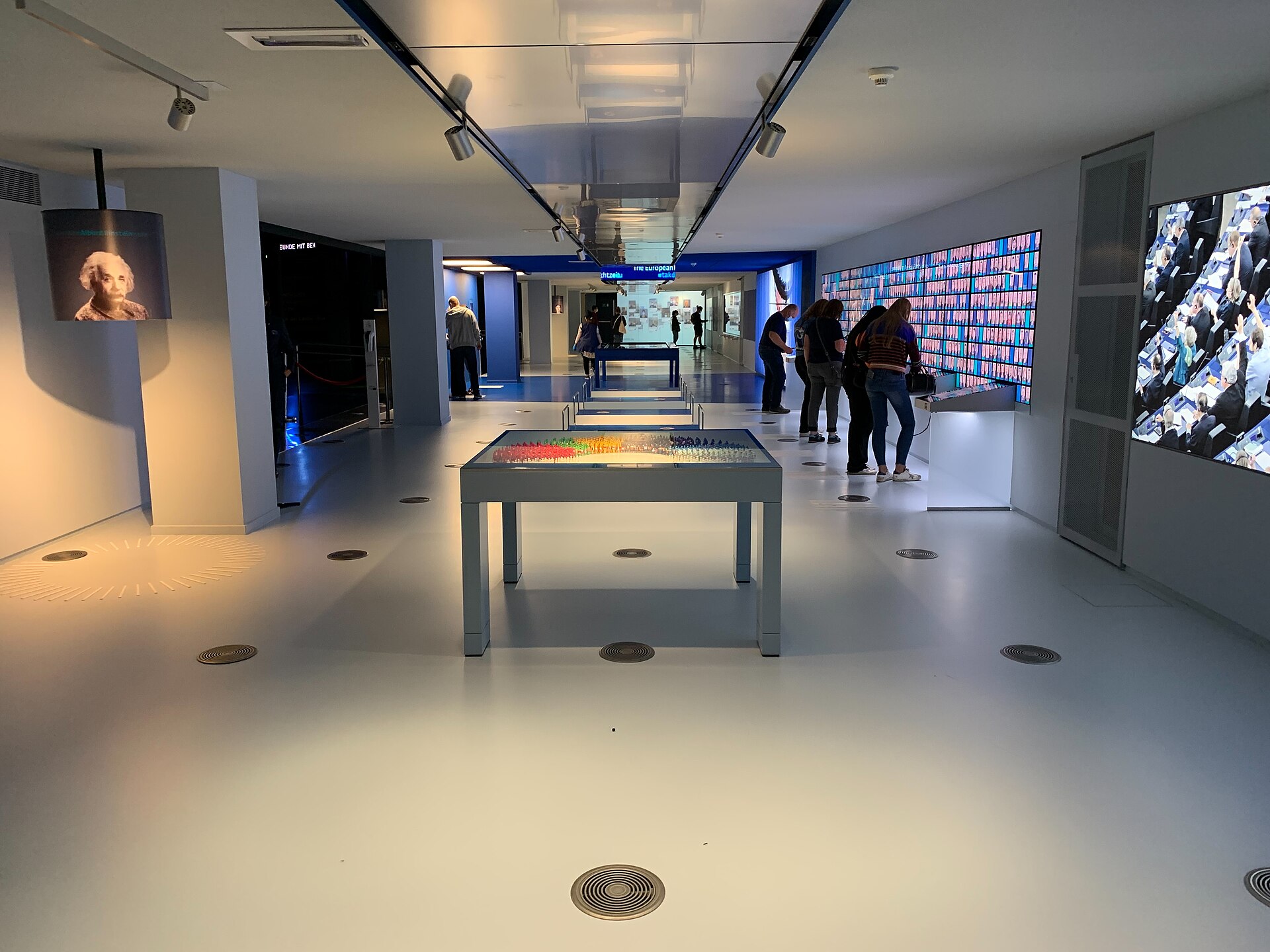 Visitors examine interactive wall displays beside a model of parliamentary seating inside the Parlamentarium exhibition in Brussels.
