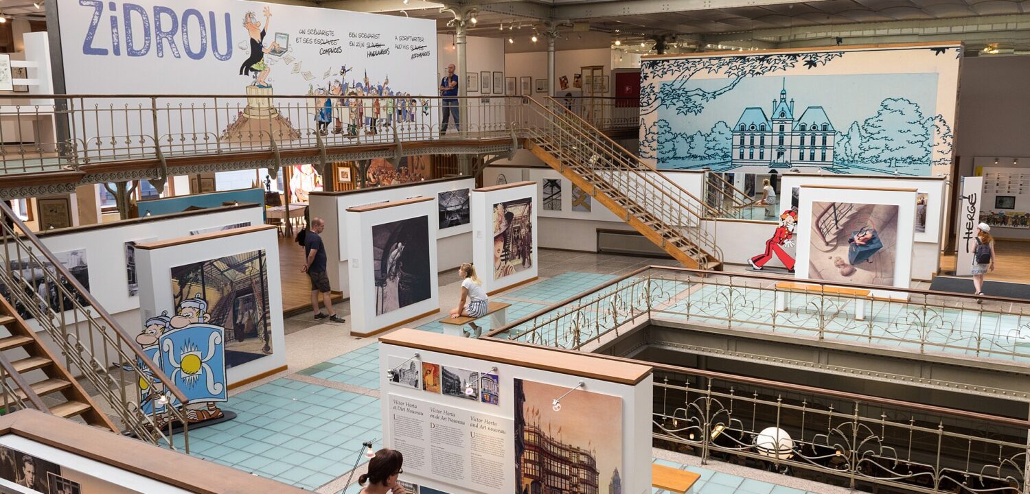Visitors explore comic exhibitions beneath the glass roof and iron galleries of the Belgian Comic Strip Centre in Brussels.