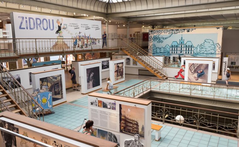 Visitors explore comic exhibitions beneath the glass roof and iron galleries of the Belgian Comic Strip Centre in Brussels.