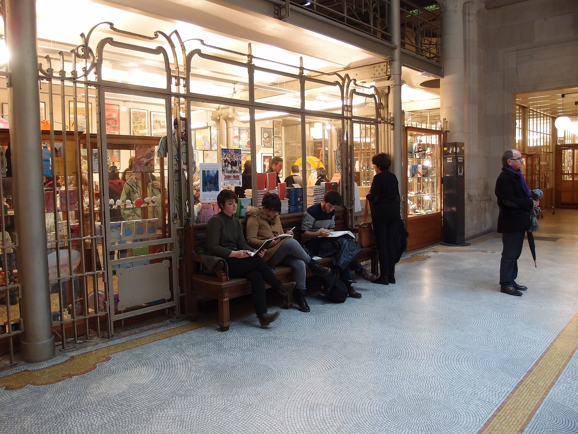 Visitors read on a bench outside the bookshop, framed by Art Nouveau ironwork inside Brussels’ Belgian Comic Strip Centre.