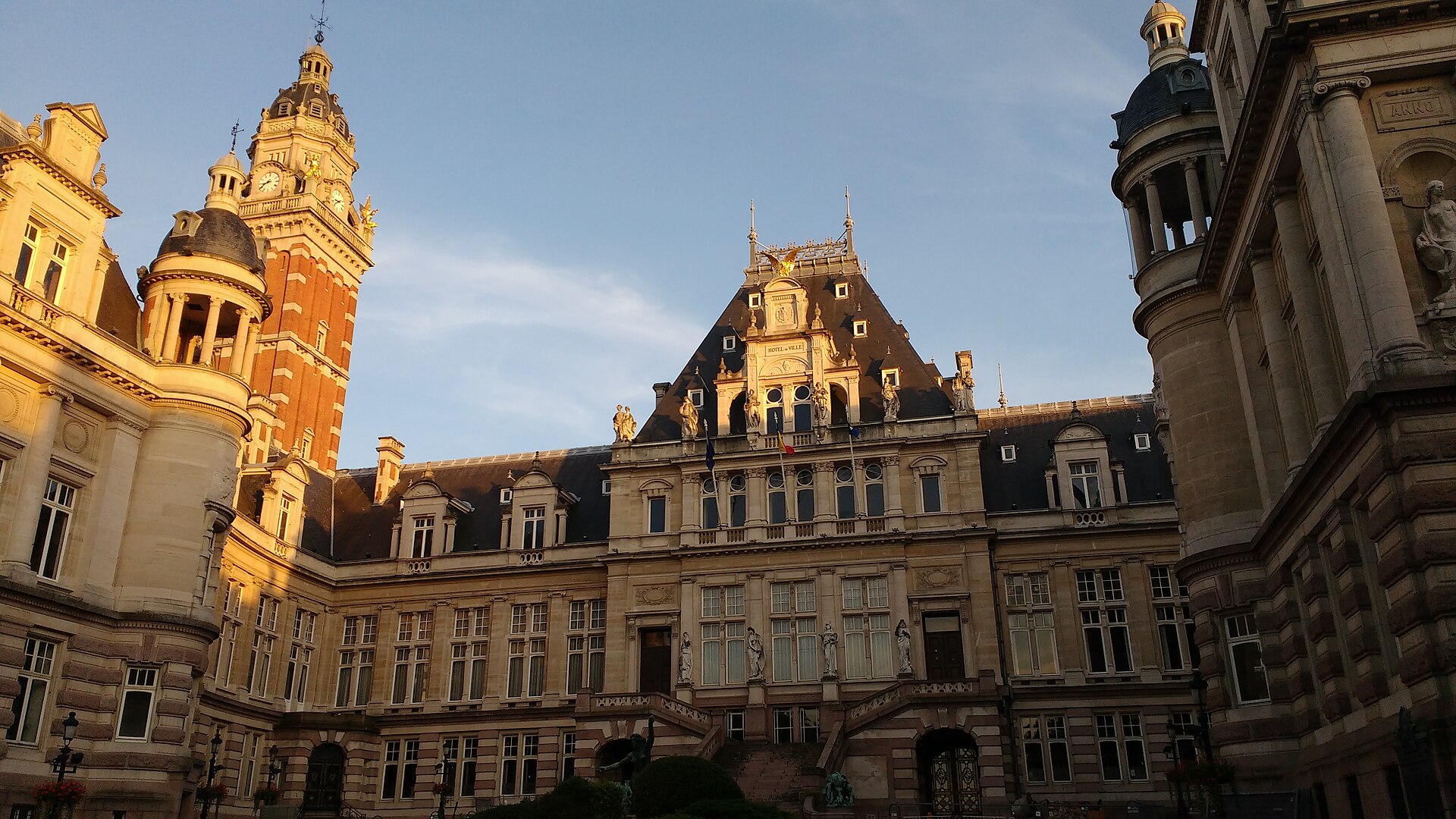 Warm evening light illuminates Saint-Gilles Town Hall in Brussels, highlighting its tower, sculpted stonework and steep slate roofs.
