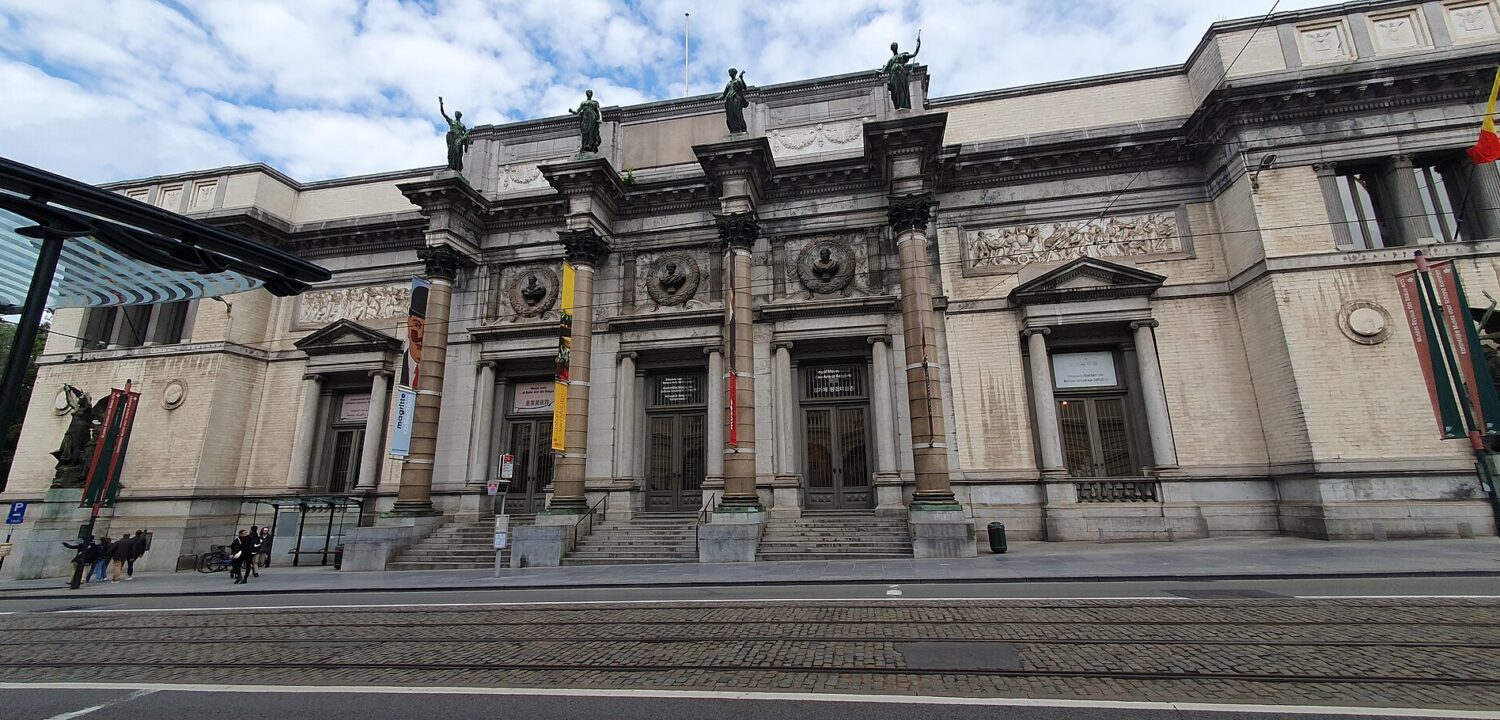 Wide view of the Royal Museums of Fine Arts of Belgium in Brussels, showing the columned entrance across cobbled tram tracks.