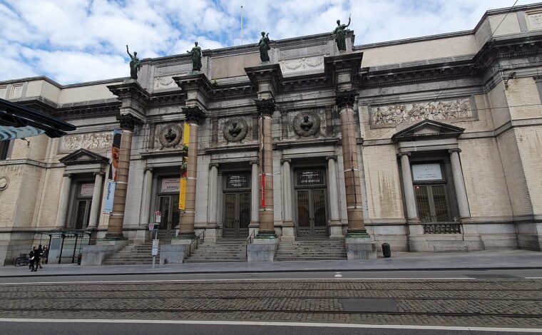 Wide view of the Royal Museums of Fine Arts of Belgium in Brussels, showing the columned entrance across cobbled tram tracks.
