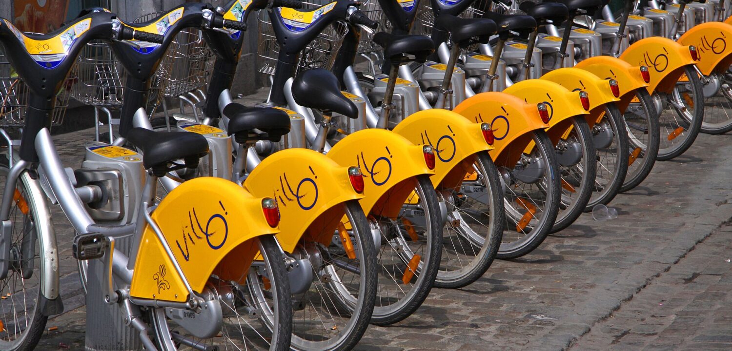 Yellow Villo! wheel guards line a row of silver shared bicycles docked on a cobbled street in central Brussels.